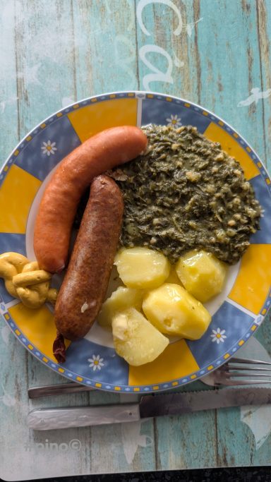 Ein Teller mit zwei Würsten, grünen Bohnen und gekochten Kartoffeln, serviert mit Senf.