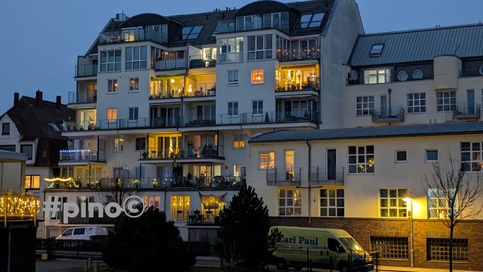 Mehrstöckiges Wohngebäude mit beleuchteten Balkonen bei Dämmerlicht.