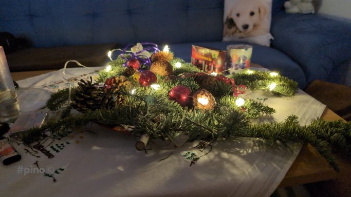 Weihnachtliche Dekoration mit Lichtern, Tannenzapfen, Kugeln und Karten auf einem Tisch.