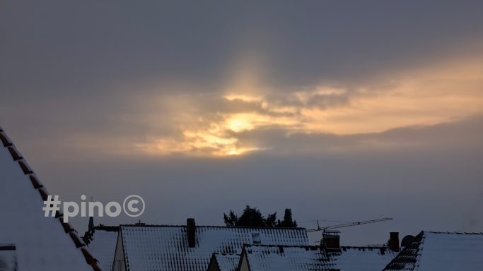 Winterliche Wolkenlandschaft mit Sonnenstrahlen hinter grauen Wolken.