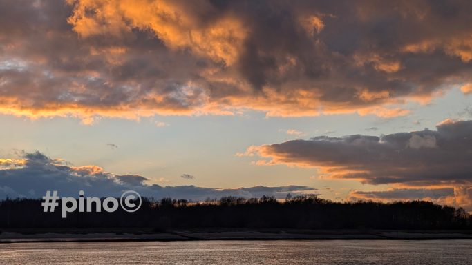 Sonnenuntergang mit Wolken und orangefarbenem Himmel über einem ruhigen Gewässer.