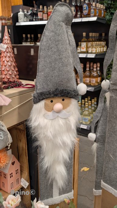 Grau behangener Nikolaus mit weißem Bart und rosa Nase, steht auf einem Tisch.