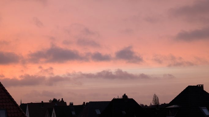 Rosa-orangefarbener Himmel über silhouettierten Dächern während der Dämmerung.