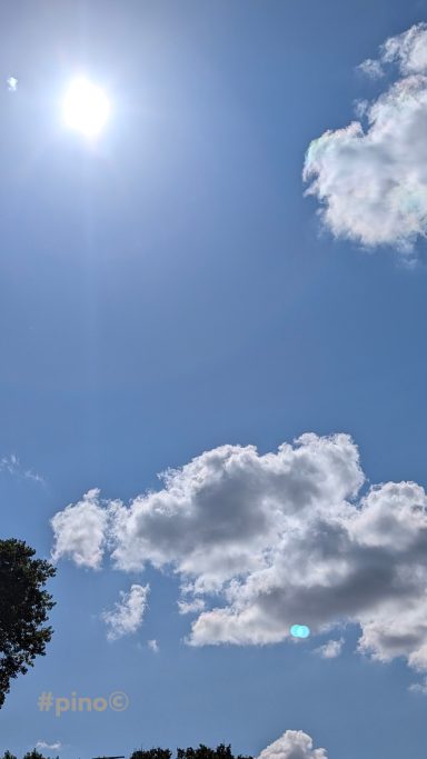 Heller blauer Himmel mit einer Sonne und einigen weißen Wolken.