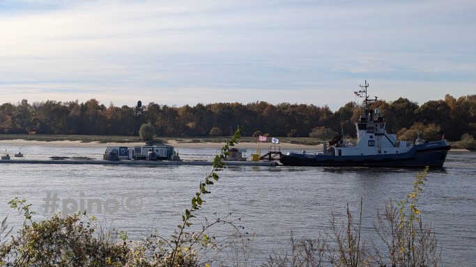 Zwei Schiffe fahren auf einem ruhigen Fluss mit Bäumen im Hintergrund.