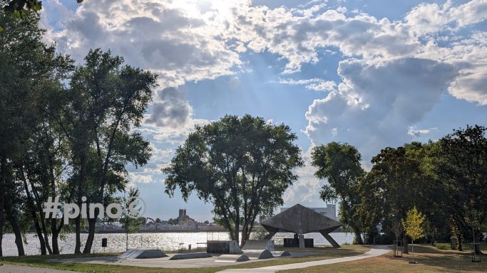 Eine ruhige Landschaft am Wasser mit Bäumen und wolkigem Himmel.