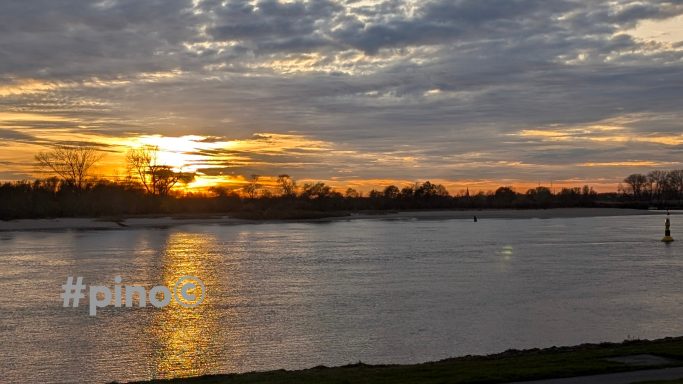 Sonnenuntergang über einem ruhigen Fluss, orange und goldene Farbtöne am Himmel.