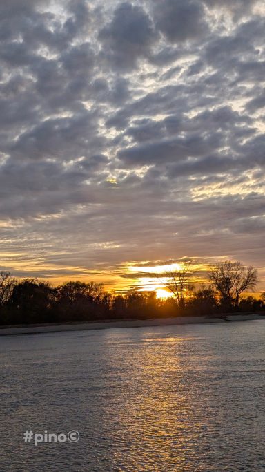 Sonnenuntergang über dem Wasser, mit Wolken am Himmel und orangefarbenem Licht.