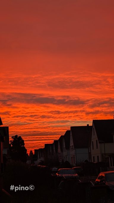 Sonnenuntergang mit roten Wolken und silhouettierten Häusern im Vordergrund.