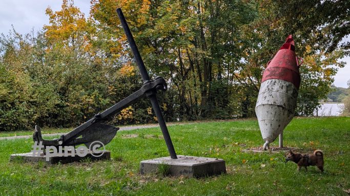 Anker und Boje stehen im Freien, umgeben von grüner Wiese und Bäumen.