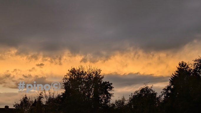 Dramatischer Himmel mit dunklen Wolken und orangefarbenem Sonnenuntergang.