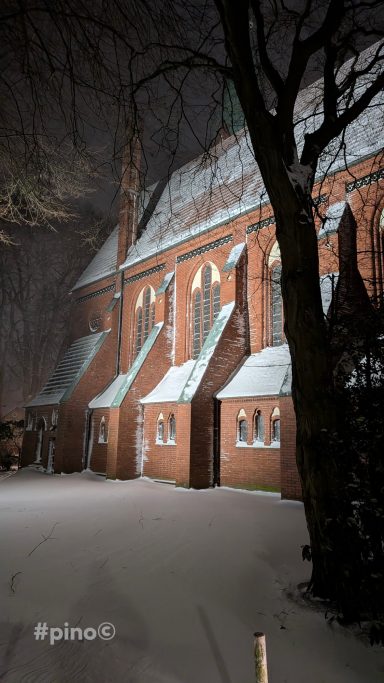 Eine neogotische Kirche im Schnee bei Nacht, umgeben von Bäumen.