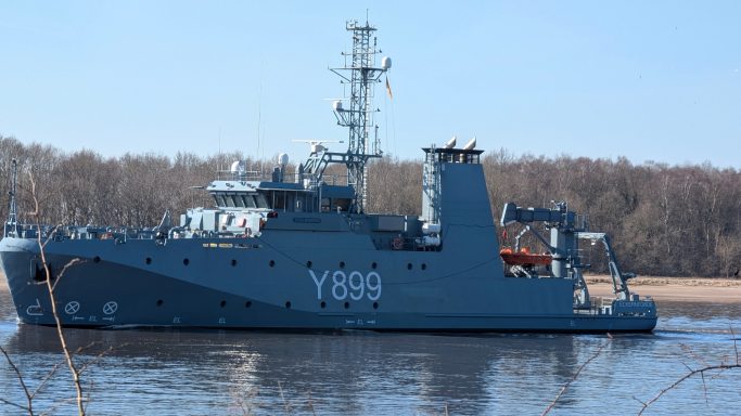 Graues Patrouillenschiff Y863 fährt auf einem ruhigen Fluss, umgeben von Bäumen.