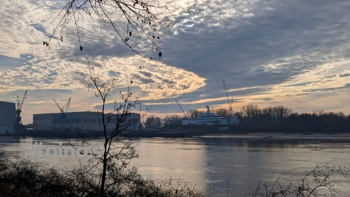 Sonnenuntergang über einem ruhigen Gewässer mit Wolken und Silhouette von Gebäuden.