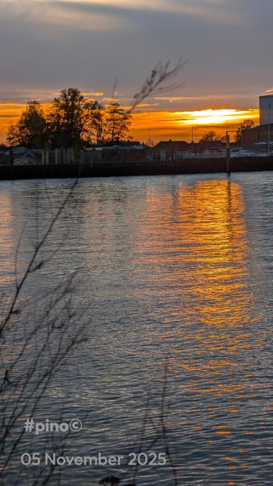 Sonnenuntergang über einem Gewässer, orangefarbene Reflexionen auf dem Wasser.