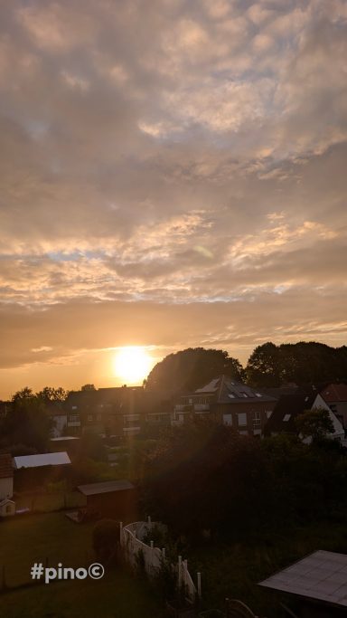 Sonnenuntergang über einer ruhigen Landschaft mit Wolken und Bäumen.