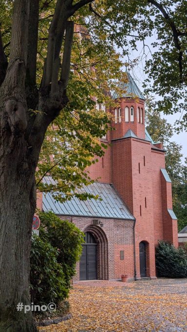 Rotbraune Kirche umgeben von Bäumen und herbstlichem Laub.
