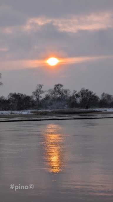 Sonnenuntergang über dem Wasser mit reflektierenden Farben und bewölktem Himmel.