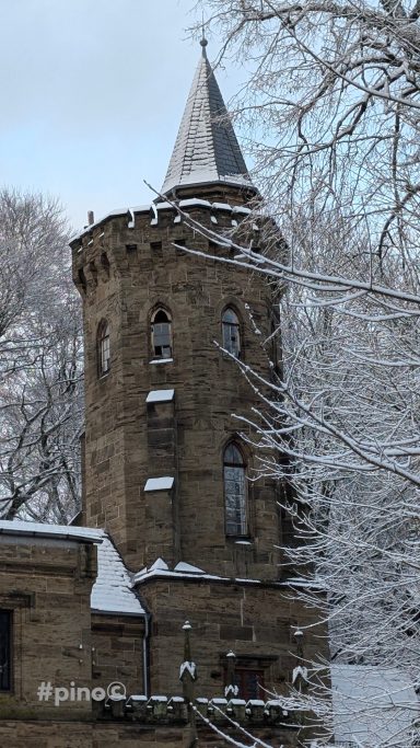 Historischer Turm einer steinernen Burg, umgeben von Schnee und Bäumen.
