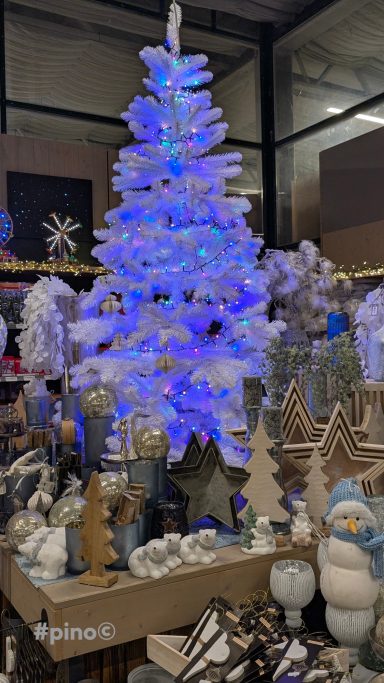 Ein dekorierter Weihnachtsbaum mit blauen Lichtern, umgeben von festlicher Dekoration.