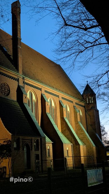 Abendliche Ansicht einer Kirche mit beleuchteten Fenstern und einem Glockenturm.