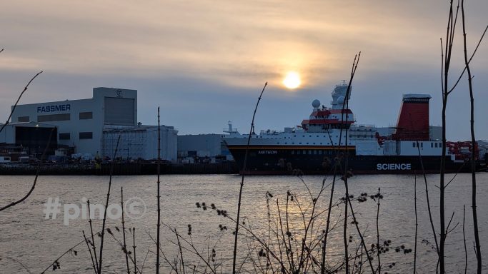 Ein Schiff liegt am Ufer unter einem bewölkten Himmel bei Sonnenuntergang.