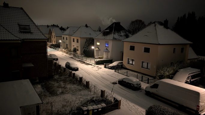 Schnee bedeckte Straße in einer ruhigen Wohngegend bei Nacht.