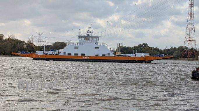 Fähre fährt über einen Fluss, umgeben von Wasser und Bäumen.