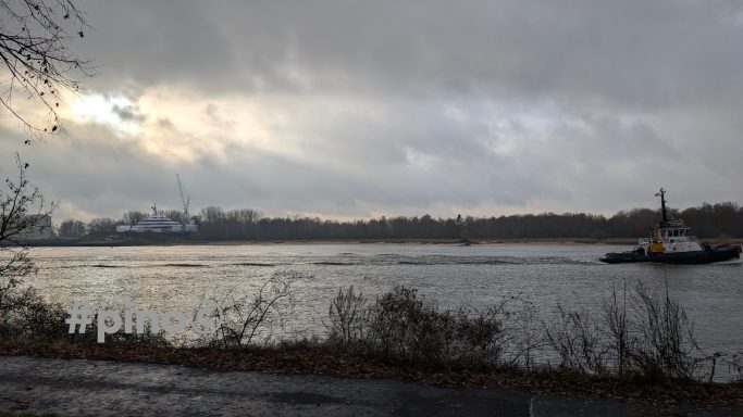 Blick auf einen Fluss mit einem Schiff und bewölktem Himmel im Hintergrund.