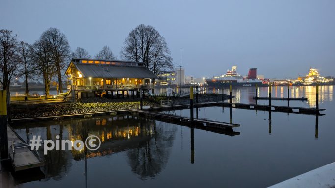 Gemütliches Restaurant am Wasser bei Dämmerung, reflektiert im ruhigen Wasser.