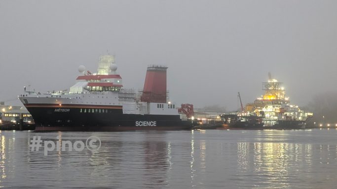 Zwei Schiffe im Nebel, reflektiert im Wasser. Ein Schiff hat eine rote und weiße Farbgebung.