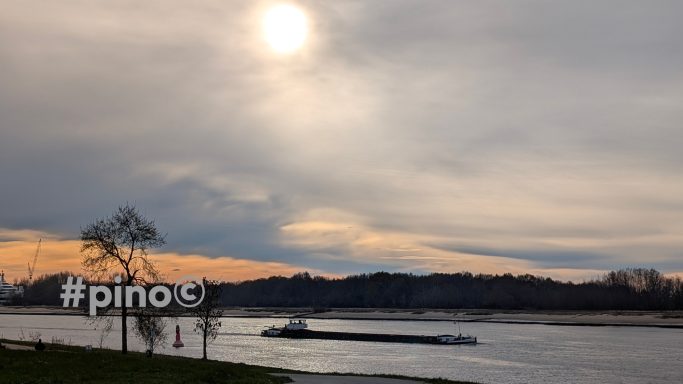 Flusslandschaft bei Sonnenuntergang, grauer Himmel und schwimmendes Boot.