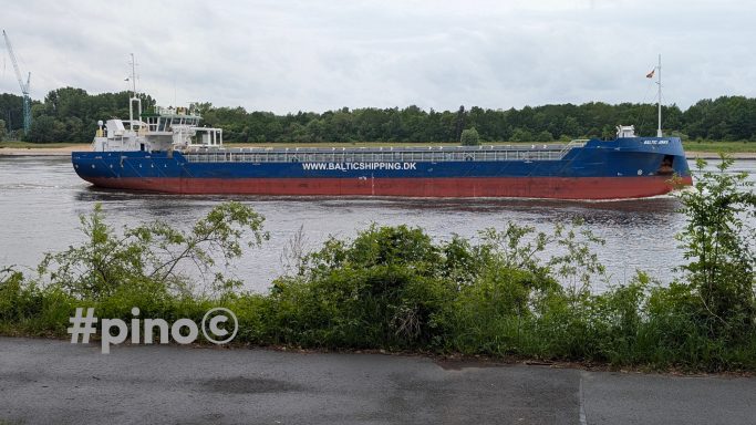 Lastkahn fährt auf einem ruhigen Fluss mit grüner Ufervegetation.
