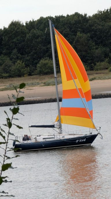 Ein Segelboot mit bunten Segeln fährt entlang eines Flusses.