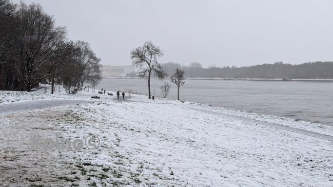 Schneebedeckte Landschaft mit Bäumen und einem Fluss im Hintergrund.