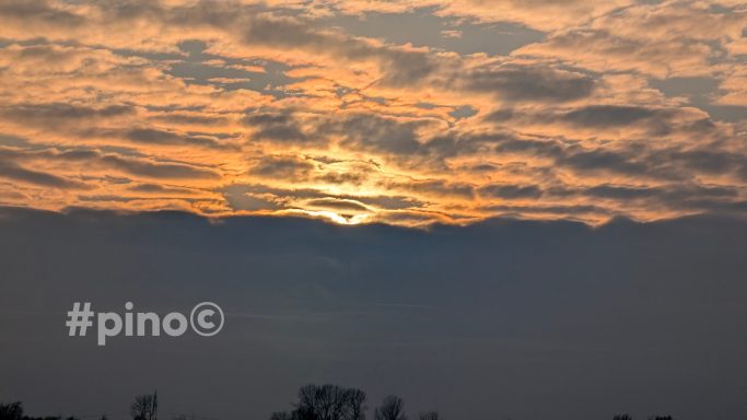 Sonnenuntergang mit Wolken und orangefarbenem Himmel über einer Stadtlandschaft.