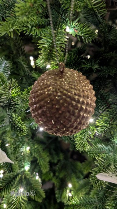 Goldene Weihnachtskugel mit schuppiger Struktur hängt an einem Tannenbaum.