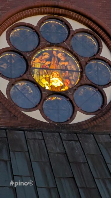 Buntglasfenster in einem runden Format mit religiösen Motiven und warmem Licht.