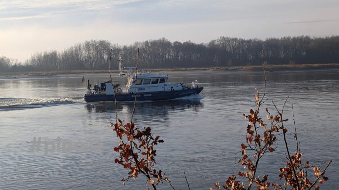 Ein Boot fährt auf einem ruhigen Fluss, umgeben von Bäumen und Nebel.