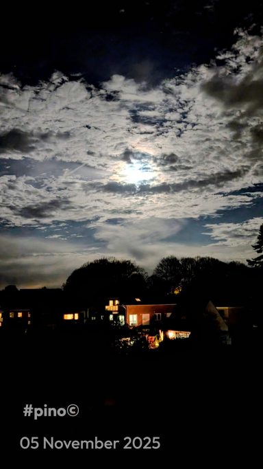 Helle Mondschein über bewölktem Himmel, darunter beleuchtete Häuser.