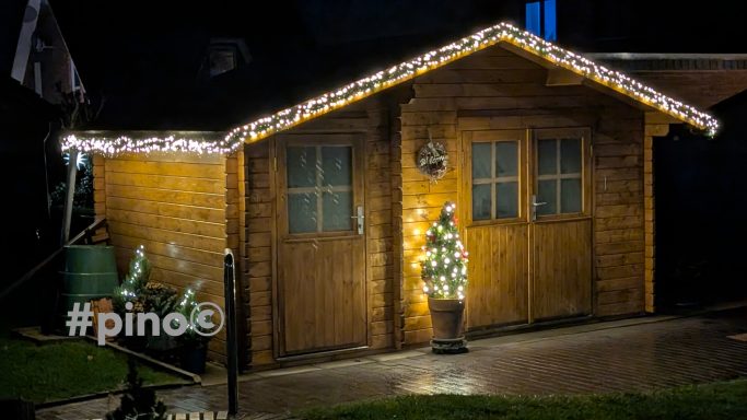 Holzhütte mit Weihnachtslichtern und einem dekorierten Weihnachtsbaum davor.
