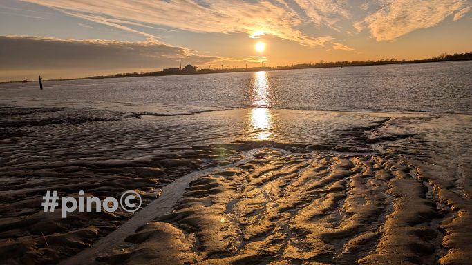 Sonnenuntergang über einem flachen Gewässer mit spiegelndem Licht und visuellen Strukturen.