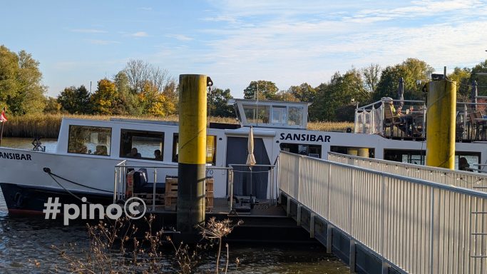Ein Passagierschiff mit gelben Schornsteinen am Ufer eines ruhigen Gewässers.