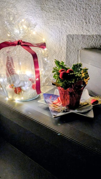 Dekorative Weihnachtsgestecke mit Lichtern und Pflanzen in warmem Ambiente.