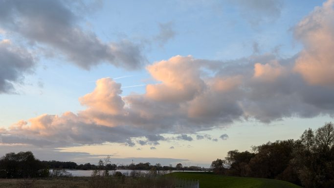 Wolkenformationen über einer Landschaft bei Sonnenuntergang, sanfte Farben am Himmel.