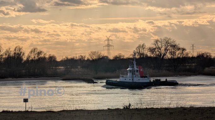 Ein Schubboot fährt auf einem ruhigen Gewässer bei Sonnenuntergang.