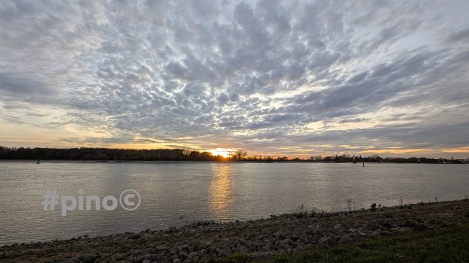 Blick auf einen Fluss bei Sonnenuntergang, umgeben von bewölktem Himmel.