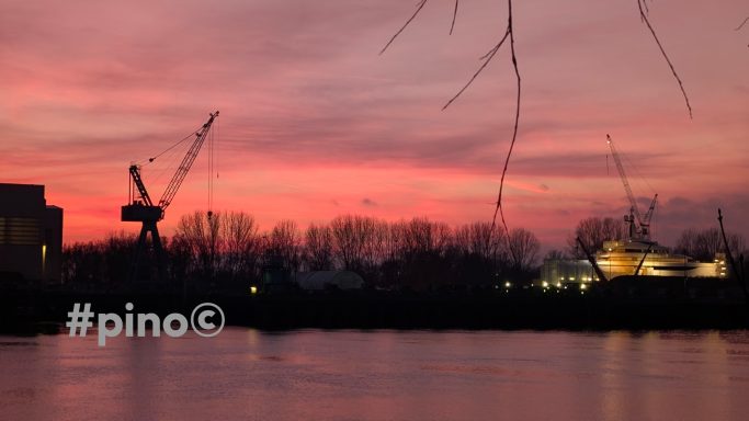 Abendhimmel mit rosa und lila Farben, Kränen und einem Wasserweg im Vordergrund.