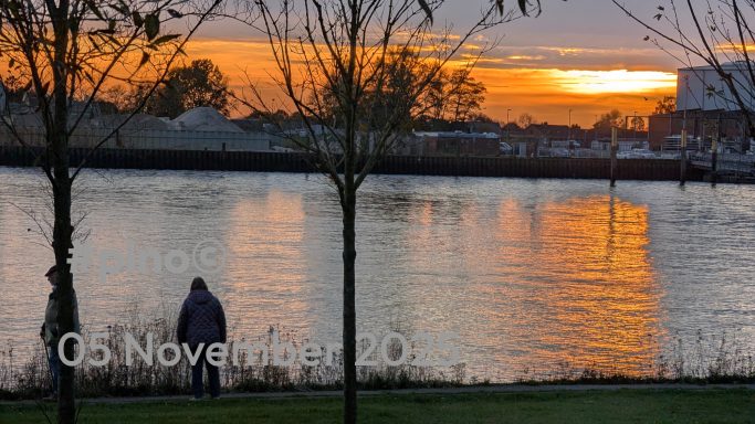 Sonnenuntergang über einem Fluss, mit silhouettierten Bäumen im Vordergrund.