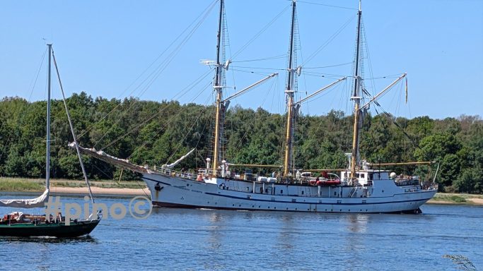 Dreimastsegler im Wasser, umgeben von Bäumen und einem kleinen Boot.